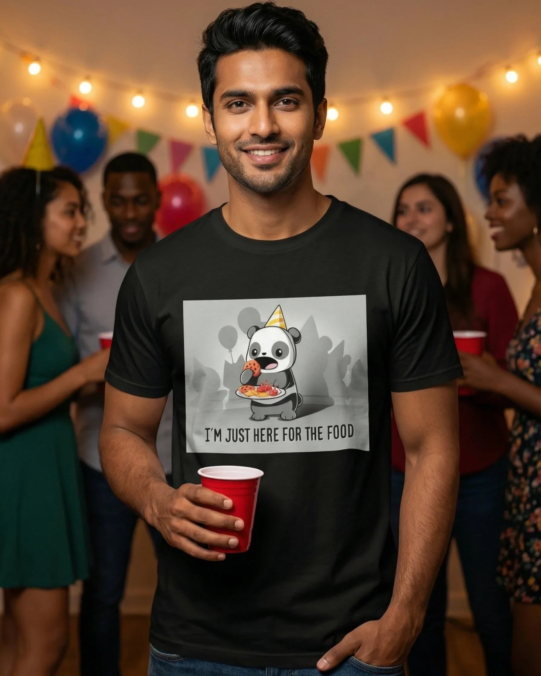 Man wearing a black t-shirt with a panda graphic and text, holding a red cup in a festive setting.